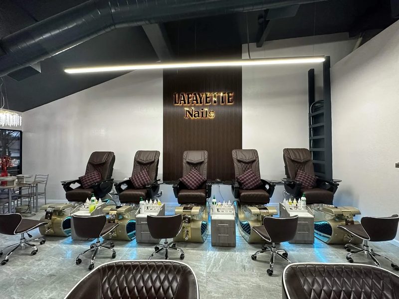 A row of five pedicure chairs facing the gold Lafayette Nails sign inside the renovated salon