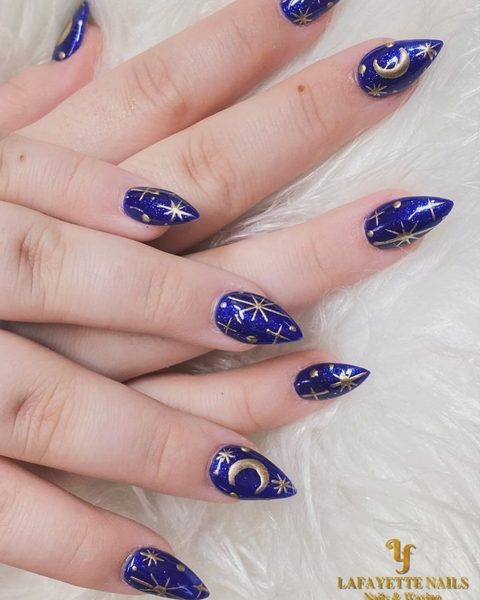 Deep navy stiletto nails with hand-painted gold stars and crescent moons